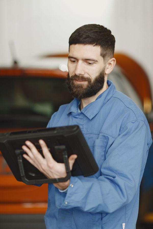 A mechanic in blue workwear reads a work order on a tablet in the workshop